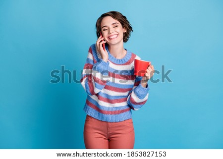 Photo portrait of laughing girl speaking on mobile phone keeping cup with drink isolated on vibrant blue color background
