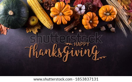 Thanksgiving background decoration from dry leaves and pumpkin on  dark stone background. Flat lay, top view with Thanksgiving text.