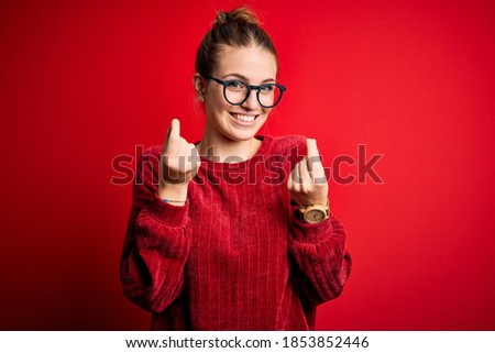 Young beautiful redhead woman wearing casual sweater over isolated red background doing money gesture with hands, asking for salary payment, millionaire business