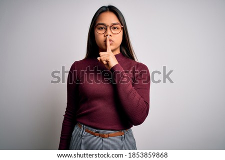 Beautiful asian business woman wearing casual sweater and glasses over white background asking to be quiet with finger on lips. Silence and secret concept.