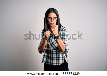 Young brunette woman with blue eyes wearing casual shirt and glasses over white background Ready to fight with fist defense gesture, angry and upset face, afraid of problem