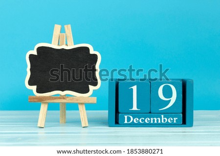 wooden calendar with the date of December 19 and an easel on a blue background, place for text, International day help the poor