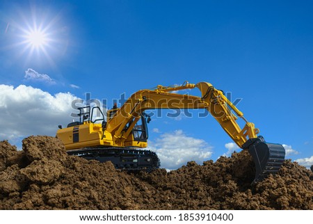 Yellow excavators are digging the soil in the construction site with the sky and sun background