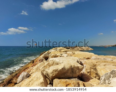 A strip of cape of large stones goes into the distance into the sea, over which a parachute flies.. High quality photo