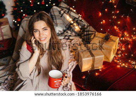 Young woman relaxing at home, enjoying Christmas time. Beautiful girl drinking tea at home, sitting near christmas tree. High quality photo
