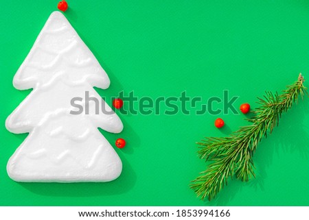 New Year's composition. Styrofoam Christmas tree, fir branches, berries on a green background. Christmas, winter, new year concept. Flat lay, top view with copy space.