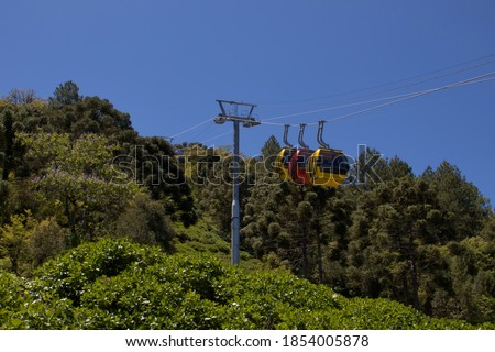 cable car with yellow and red cabins, gliding over the lush vegetation of Caracol Park, under a cloudless blue sky - CANELA, RS, BRAZIL.