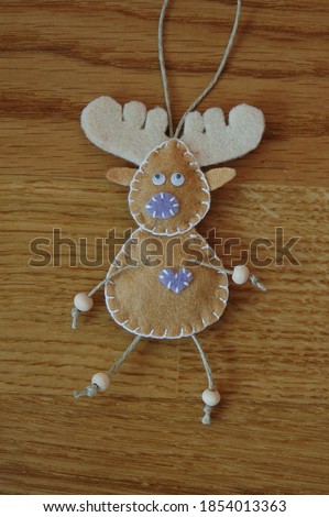 A reindeer close up with a purple nose and heart, on a wooden background. Felt Christmas hand sewn unique decorations.