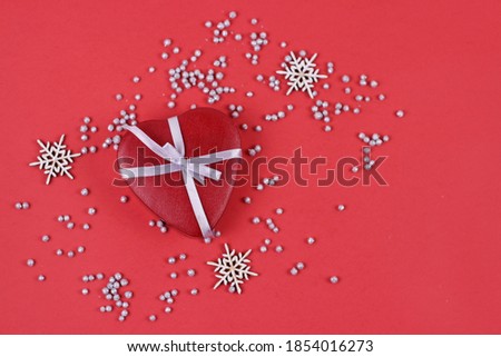 Merry Christmas and Happy New Year greeting card. xmas red gift box in form heart with white ribbon and snowflakes on red background.Flat lay with copy space.