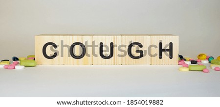 The word COUGH is made of wooden cubes on a grey background with pills. Medical concept.