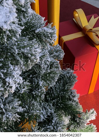 Picture of Christmas tree covered with snow and a gift behind the Christmas tree.