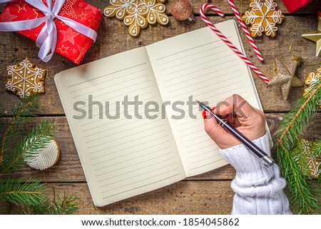 Woman hands write Christmas letter, wishlist or To Do list on notepad paper on wooden background with Christmas decoration, top view flatlay copy space