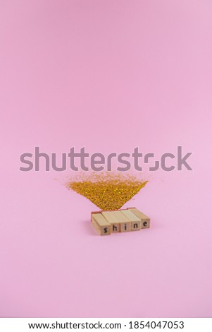 Word shine, written on a wood blocks with shining gold glitters behind, on a pink background. Close focus on a word shine with sparkling triangle shape behind. Concept women day celebration photo.