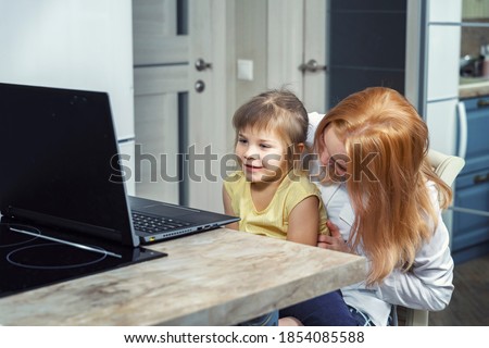 Mother and daughter using laptop and Internet. Freelancer workplace in home kitchen. Concept for womens business, working mom, freelance, home office. family lifestyle.