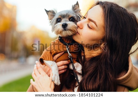 Cute woman kissing a cute little dog, close up portrait. Lady hugs a biewer terrier dog on the street. Love of woman owner and pet.