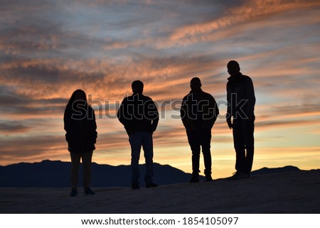 Group of four friends standing at sunset time on background mountains and colorful clouds pattern