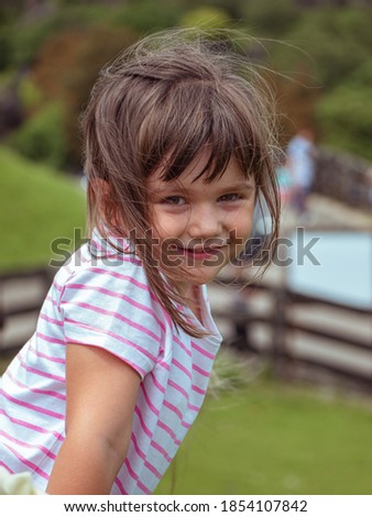 Smiling girl with a pink and white striped t-shirt leaning on a fence while the wind moves her hair in the Cabarceno natural park in Cantabria