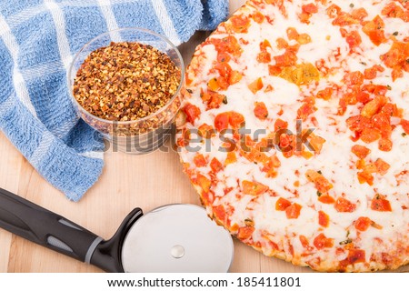 Fresh, hot tomato pizza on a wood cutting board with cutting wheel, hot pepper flakes, and a blue towel