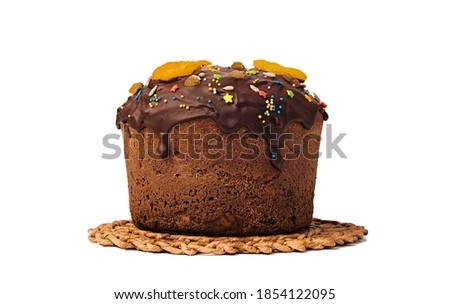 Sweet cake, filled with chocolate and decorated with dried fruits, dried apricots, candied fruits, cherries, raisins, as well as hazelnuts, almonds and seeds, stands on wicker straw stand. Isolated.