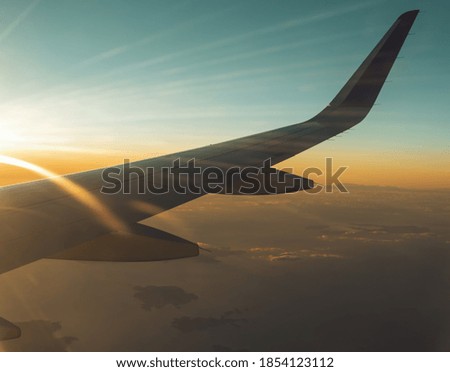 View from plane window at airplane wing and cloudy landscape during sunset.