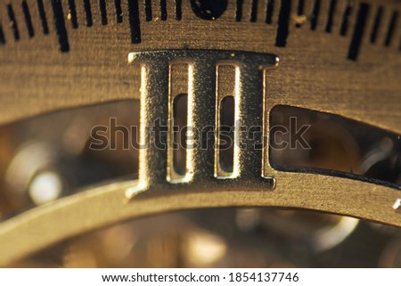 Macro photograph of the Roman numeral three on the inner dial of a bronze wristwatch. Conceptual image of time. Selective focus.
