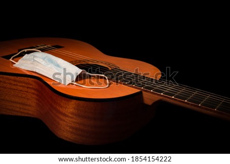 Acoustic Guitar Body with a Face Mask Close Up on a Black Background. This studio shot is a concept for face mask mandate due to covid-19, coronavirus restrictions for performing musicians. Royalty-Free Stock Photo #1854154222