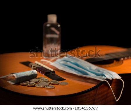 Acoustic Guitar Body with Face Mask, Hand Sanitiser and Cash. Close up studio shot concept for musicians loss of earnings, or restrictions / requirements for gigging performance. Royalty-Free Stock Photo #1854156769