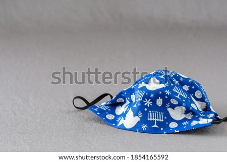 Handmade fabric mask on a silver background, celebrate Hanukkah with Jewish symbols on a blue mask
