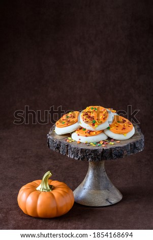 Fall harvest, orange frosted sugar cookies with colorful sprinkles, on a wooden cake stand, orange ceramic pumpkin
