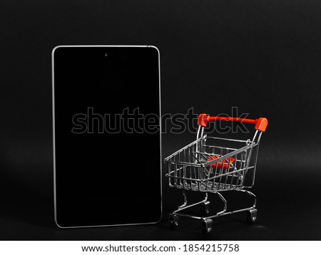 A tablet and shopping cart on black background, a blank for the design, concept. Copy space.