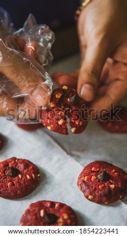 Close up hand with disposable glove cracking a homemade red velvet cookies with almond and chocolate chips on baking tray. Selective and soft focus. Commercial photography concept.