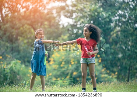 Cute african american and Asian little girl playing outdoor. Friends happy playing with bubbles together.