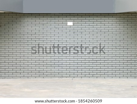 Light gray brick wall with a gray panel above and a concrete pavement in front. Background for copy space