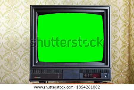 Antique TV with green screen on an antique wooden cabinet, old design in a house in the style of the 1980s and 1990s.