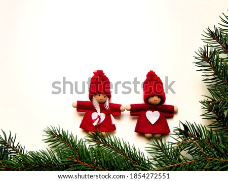 Christmas decorative background for greeting card, spruce twigs with two wooden Christmas elves girl and boy in a red dress with a white heart and a knitted hat