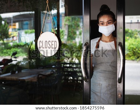Thai girl waitress with protective face mask standing at  restaurant doorway. Thailand, Koh Phangan 