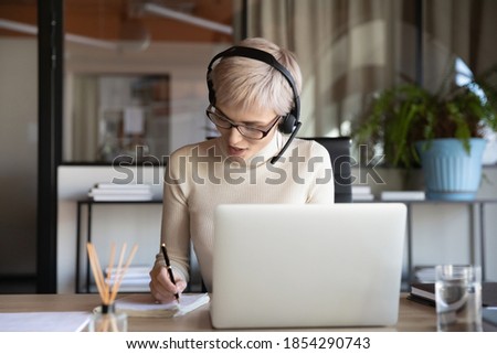 Businesswoman wearing headset writing notes, using laptop in office, female employee intern watching webinar, studying, manager consulting client online, making video call, internet negotiations