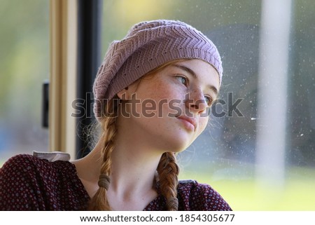 Portrait of a young dreamy freckled girl with pigtails dressed in retro style clothes in a wagon of a driving tramway. Transportation and lifestyle concept.

