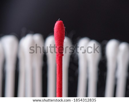 White cotton swabs on a black background. One of them is red. Symbolizes a person who is different from the crowd. Macro.