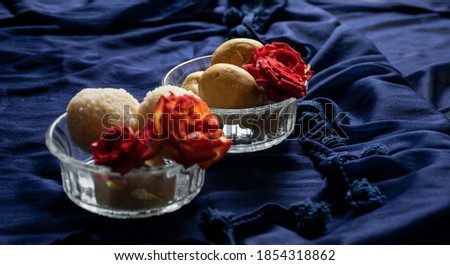 Picture of delicious besan laddu decorated in bowl with fresh red roses in a blue background. Besan laddus made during diwali festival in India.