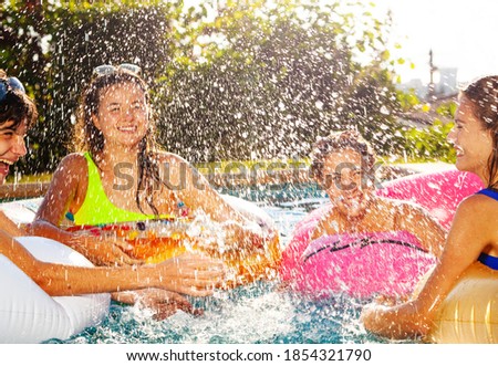 Group of children play laughing in swimming pool splashing with inflatable toys together