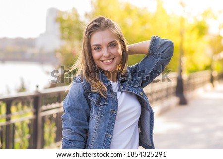 Portrait of a happy and attractive blonde Caucasian young woman in a casual denim jacket outdoors in a park on a sunny autumn day. A concept of lifestyle, happiness and joy. Royalty-Free Stock Photo #1854325291