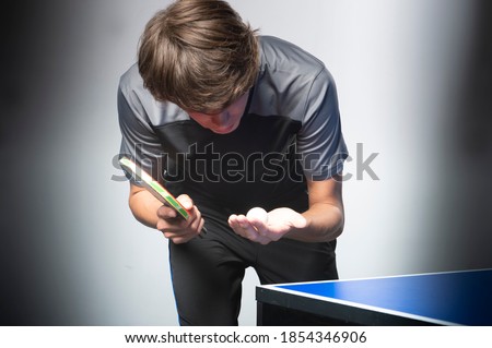 Portrait of young man playing tennis on black background. Table tenns player serving 