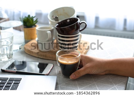 A young female freelancer  working from home holding a cup of coffee with many cups in the background drinks too much coffee caffeine addiction anxious and crazy in maniac bad lifestyle concept Royalty-Free Stock Photo #1854362896