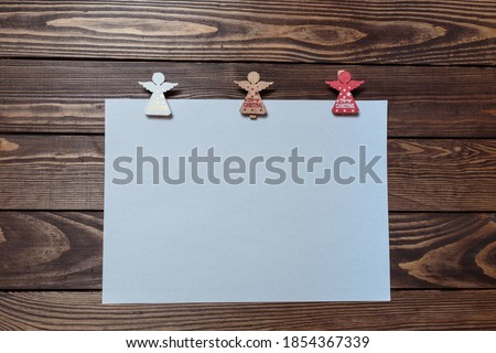 christmas card. white blank sheet on a wooden table. three wooden figurines of angels. letter for santa claus. advertising poster. layout. mockup.