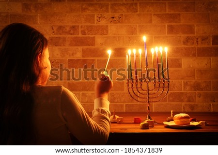 Low key image of jewish holiday Hanukkah background with girl looking at menorah (traditional candelabra) and burning candles Royalty-Free Stock Photo #1854371839