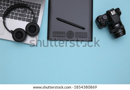 Workspace of a photographer or retoucher. Laptop, graphic tablet, camera and headphones on a blue background. Top view. Copy space