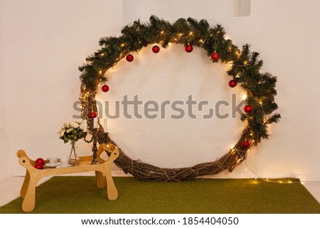 Christmas photo zone, lights, Christmas tree, huge New Year's wreath, tray with flowers, cups and candles. Green carpet, imitation of grass. Studio.