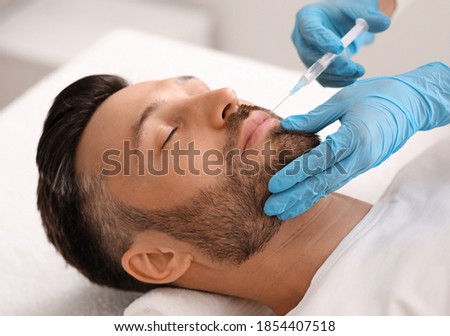 Attractive bearded man visiting aesthetic clinic, getting lips filler, closeup. Middle aged businessman having beauty injection at male spa salon. Face care, anti-aging treatment for men concept Royalty-Free Stock Photo #1854407518