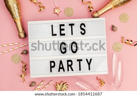 Stylish festive party decor in golden color on pink background and lightbox with text Let's go party. Flay lay